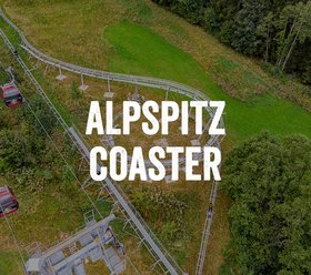 AlpSpitz Coaster Luftaufnahme der AlpSpitz Coaster-Bahn, die sich durch eine grüne Wiese und einen Wald schlängelt.