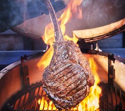Gegrilltes Tomahawk-Steak über offenen Flammen Ein großes Tomahawk-Steak wird über einem offenen Grill mit hohen Flammen gegrillt.